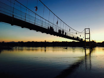 Silhouette bridge over river against sky at sunset