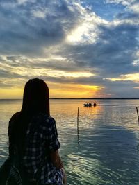 Rear view of woman standing by sea against sky during sunset