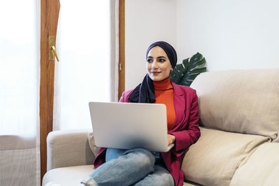 Young woman using laptop while sitting on sofa at home