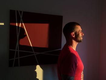 Side view of young man looking away against wall