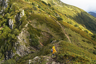 Rear view of young woman in yellow hoodie with backpack hiking in picturesque mountain valley 