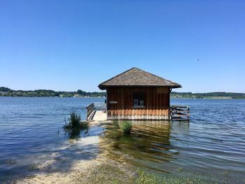 House by lake against clear blue sky