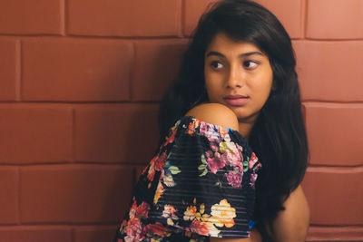 Portrait of young woman standing against brick wall