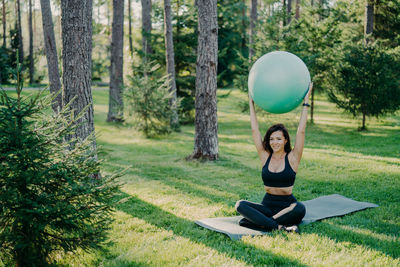 Woman with arms raised carrying fitness ball in park