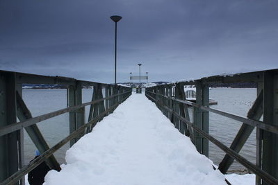 Pier over frozen lake against sky during winter