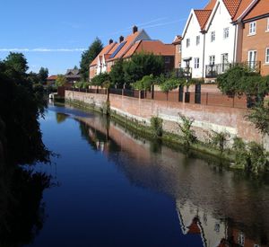 Canal by houses against sky