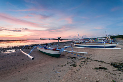 Boats moored on beach against sky during sunset