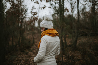 Rear view of woman standing by tree in forest during winter