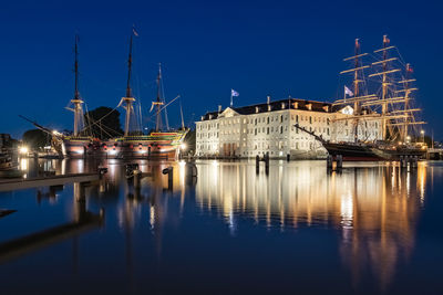 Sailboats moored in illuminated city against clear blue sky at night