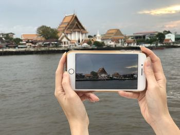 Midsection of person photographing with mobile phone in water