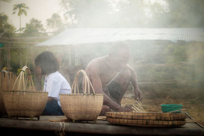 Schoolgirl studying while sitting with grandfather making wicker baskets