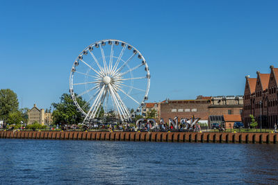 Ferris wheel by river against buildings in city