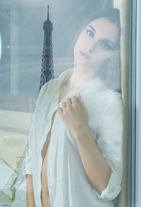 Portrait of beautiful woman seen through glass window with reflection of eiffel tower