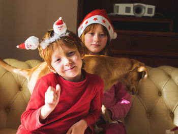 Portrait of cute sibling wearing santa hat with dog sitting at home