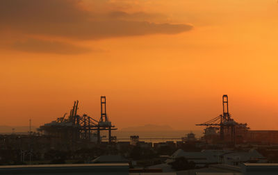 Cranes at harbor against orange sky