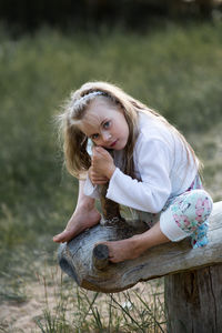Portrait of girl sitting on wooden structure at field