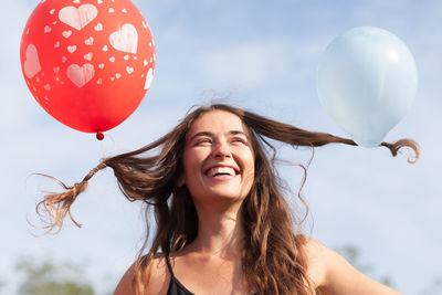 Smiling young woman with balloons against sky