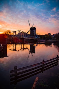 Silhouette cranes by lake against sky during sunset