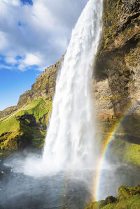 Beautiful seljalandsfoss with rainbow flowing from mountain against cloudy sky
