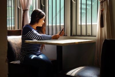 Young woman using mobile phone at table