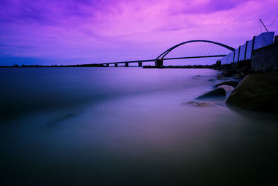 Bridge over river against sky at sunset