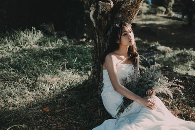 Woman with bouquet while sitting on field in forest