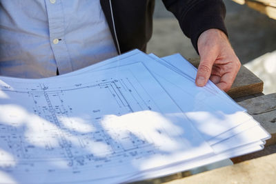Midsection of architect with blueprints at table on sunny day
