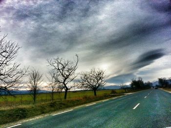 Empty road passing through field against cloudy sky