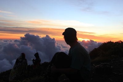Silhouette man sitting on rock against sky during sunset