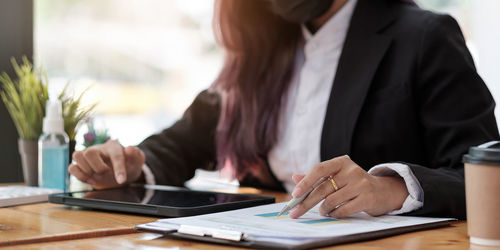 Midsection of woman using smart phone while sitting on table