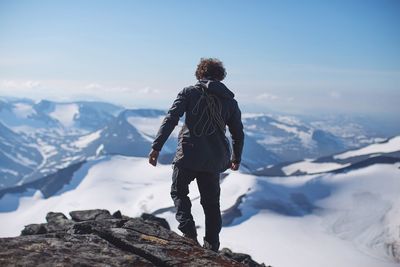 Rear view of man standing on rock against mountains