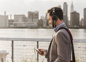 Usa, new york city, young man with headphones and cell phone at east river