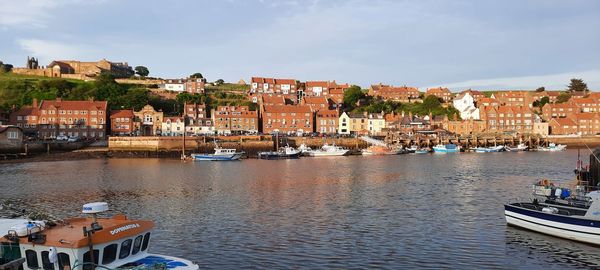 Boats moored in river by town against sky