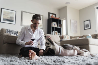 Full length of man with wineglass relaxing by dog on rug at home