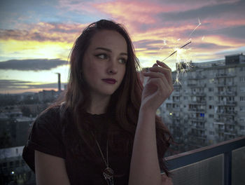 Beautiful young woman against sky during sunset