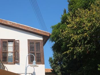 Low angle view of trees and building against clear blue sky