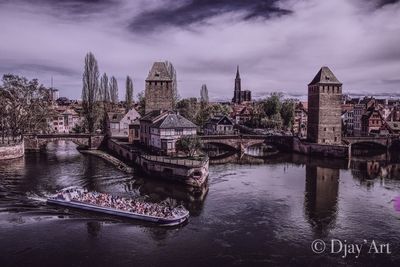 Bridge over river in city against cloudy sky