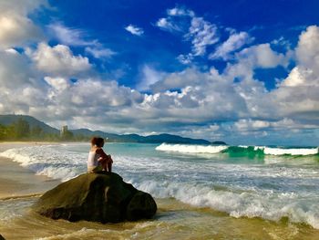 Man sitting on rock at beach against sky