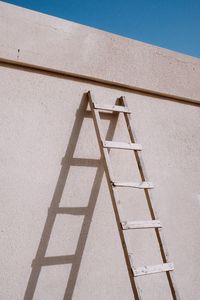 Low angle view of ladder on building wall during sunny day