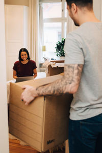 Man carrying box towards woman sitting in bedroom