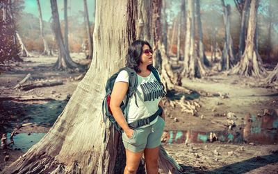 Full length of woman standing by tree trunk in forest