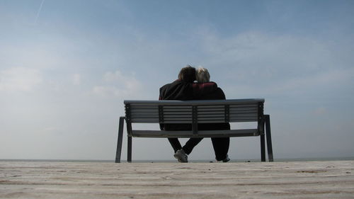 Rear view of senior couple sitting on bench at beach