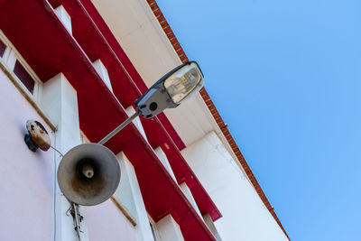 Low angle view of light post and siren against clear blue sky