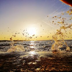 Silhouette of splashing on beach against sky during sunset