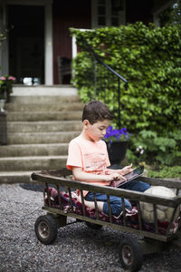 Boy using digital tablet while sitting in cart against house