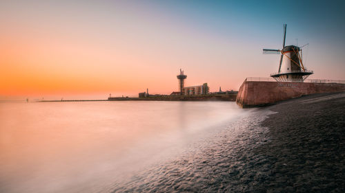 Traditional windmill at beach against sky during sunset