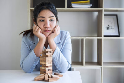 Depressed businesswoman with stacked wooden blocks on table sitting in office