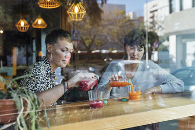 Young women pouring drink in glass while sitting by restaurant window