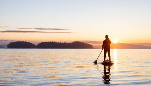 Silhouette man standing in sea against sky during sunset