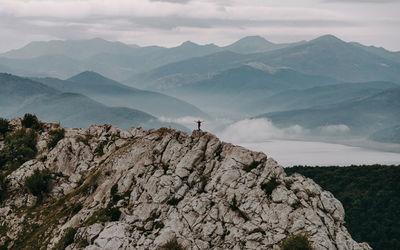 Scenic view of mountains in the background with man on top of mountain agaisnt cloudy sky